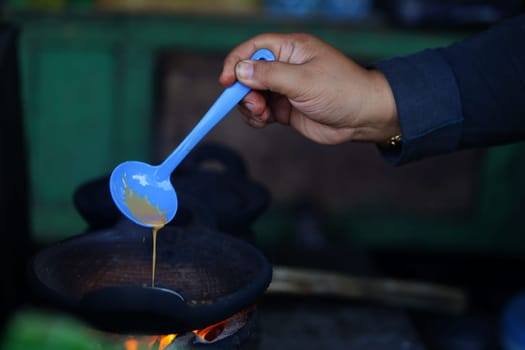 a hand holding a cooking spoon pouring on a traditional pan.