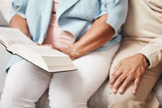 Hands, bible and praying with a senior couple reading a book together in their home during retirement. Jesus, faith or belief with a man and woman in prayer to god in a house for spiritual bonding