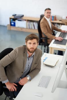 Take another look at modern business. High angle view of a serious businessman looking up at the camera in a shared office space.