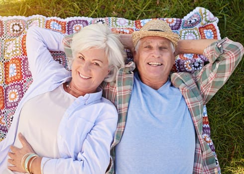 Portrait, picnic and an elderly couple lying on a blanket in a field together for romance or bonding from above. Relax, smile and retirement with happy seniors outdoor in the countryside for dating.