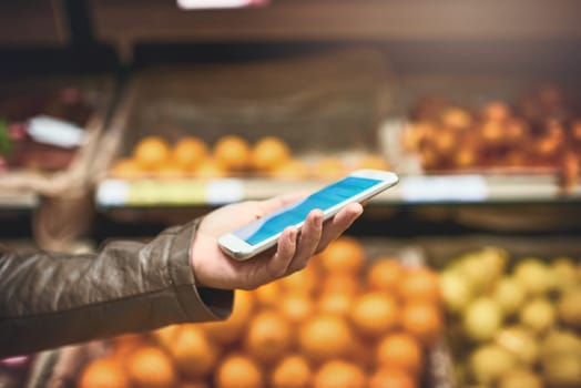 Cropped shot of a woman using a mobile phone in a grocery store.