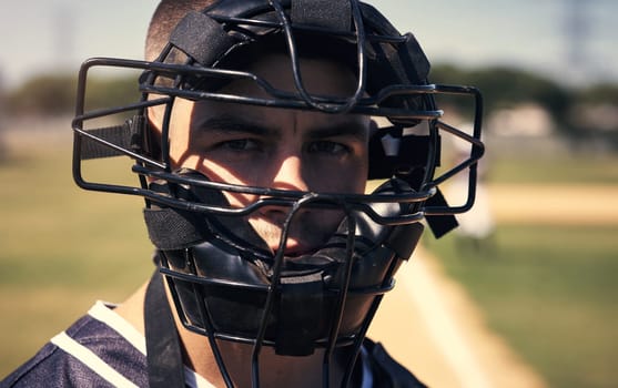 Because nobody likes getting smashed by a ball. Portrait of a young man wearing a catchers helmet while playing a game of baseball.
