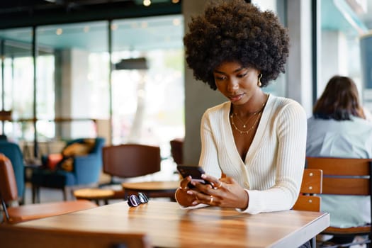 Young afro woman using mobile phone at coffee shop