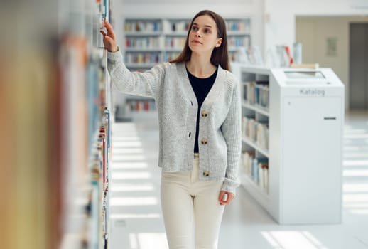 Woman, student and library for books, knowledge or learning at the university for education. Female looking at bookshelf in study, assignment or project for higher education or college scholarship