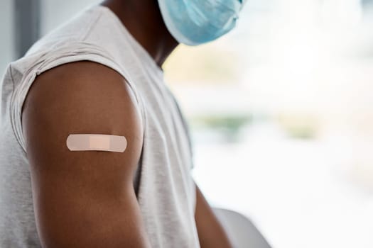 Closeup, bandage and covid vaccine for black man with mask for healthcare, wellness or safety. Man arm, plaster and vaccination for covid 19 in hospital, clinic or office for health, medicine or care