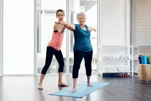 Yoga allows her to reach better health and wellness. a fitness instructor helping a senior woman during a yoga class.
