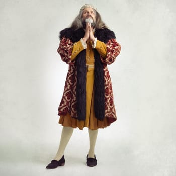 Ancient king man, praying and studio with faith, worship and renaissance fashion by backdrop. Medieval royal leader, clothes and religion with crown, prayer and robe for power, success and gratitude