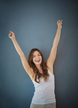 Positivity always wins in the end. Studio shot of a young woman raising her arms in triumph against a gray background.