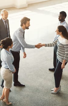 Welcoming a new member to the team. High angle shot of businesspeople shaking hands while standing in an office lobby.