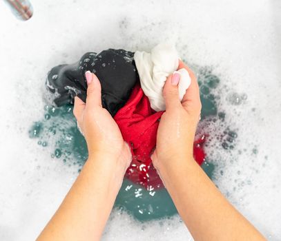 Red, black and white clothes in basin with detergent foam