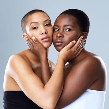 The gentle touch of the face. Portrait shot of two beautiful young women holding each others face while standing against a grey background.