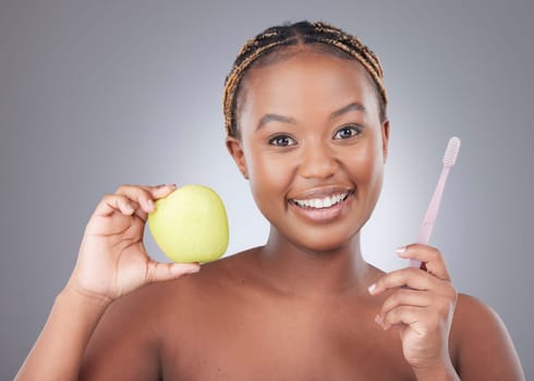 An apple a day keeps cavities away too. Studio shot of an attractive young woman brushing her teeth while holding an apple against a grey background