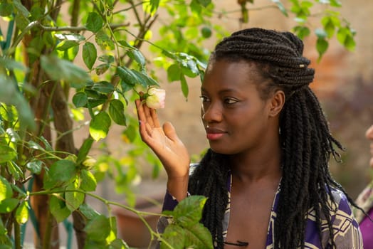 Portrait Young beautiful relaxed african woman wearing summer outfit in the garden enjoy flowers, dreadlock hairtstyle.