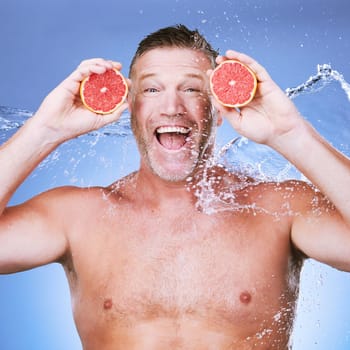 Excited man, grapefruit in hands and water in portrait, beauty skincare, eco friendly and vegan cosmetics on blue background. Hydration, vitamin c and hygiene, senior male smile and citrus fruit