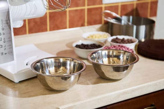 Metal bowls on a kitchen countertop with electric food processor and ingredients