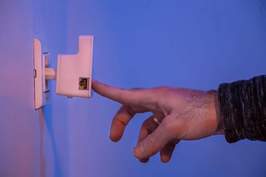 Man press with his finger on WPS button on WiFi repeater which is in electrical socket on the wall
