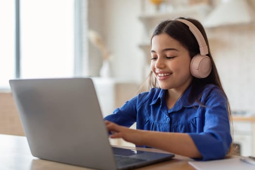 Schoolgirl Studying Online Typing On Laptop Wearing Earphones At Home