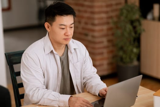 Focused middle aged asian man using laptop, working online from home, having online business meeting, copy space
