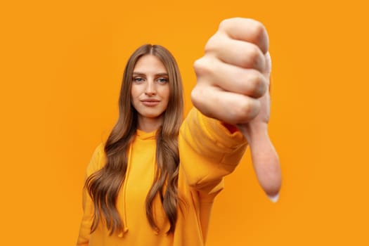 Portrait of displeased woman showing thumb down on yellow background