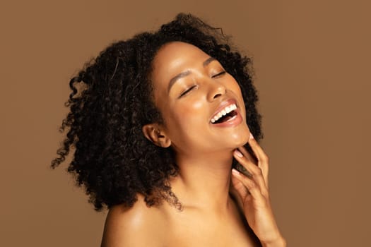 Laughing sensual half-naked black lady touching her chin, brown background