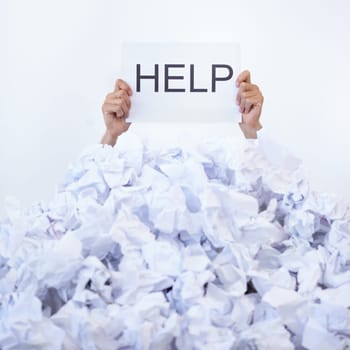 Help me. a businessman holding a help sign while buried under a pile of crumpled up paperwork.