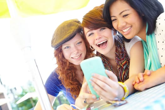 Technological fun. A group of adolescent girls laughing as they look at something on a smartphone screen.