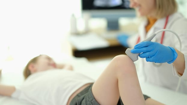 Doctor traumatologist making ultrasound examination of knee joint to child in clinic closeup
