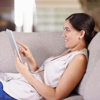 Happy woman, tablet and relax on living room sofa for streaming, browsing or social media at home. Female relaxing on technology for online entertainment, app or research lying on lounge couch.