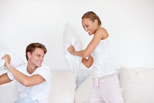 Love, pillow fight and couple being playful on the bed in the hotel room on a romantic weekend trip. Happiness, laughing and young woman and man playing together in the morning in the bedroom at home