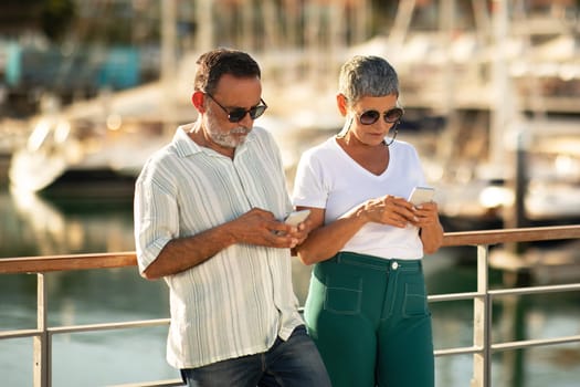 Mature Couple Using Phones Booking Yacht Cruise Standing At Marina