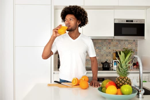 Happy African Man Drinking Orange Juice From Glass In Kitchen