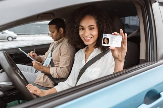 Joyful Middle Eastern Woman Showcasing Driving License Through Car Window