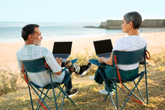 Mature Spouses Working Online On Laptops Near Ocean, Rear View