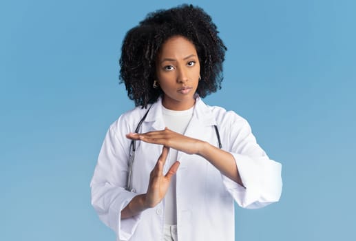 Angry unhappy confident millennial african american woman in white coat with stethoscope doing time out