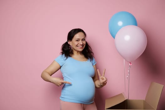 Amazed pregnant woman, expecting twins, shows two fingers looking at camera, isolated pink backdrop. Gender reveal party