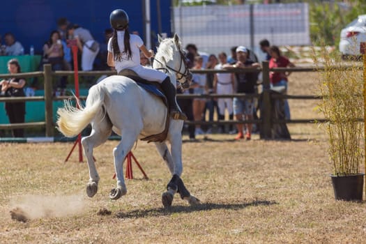 Equestrian sport - a girl in uniform riding white horse at the ranch
