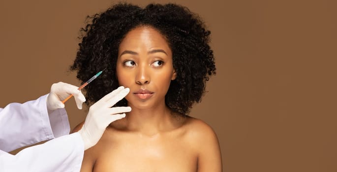 Closeup of beautiful millennial african american topless woman have beauty injections session, beautician or doctor wearing medical gloves holdng syringe next to patient face, panorama, copy space
