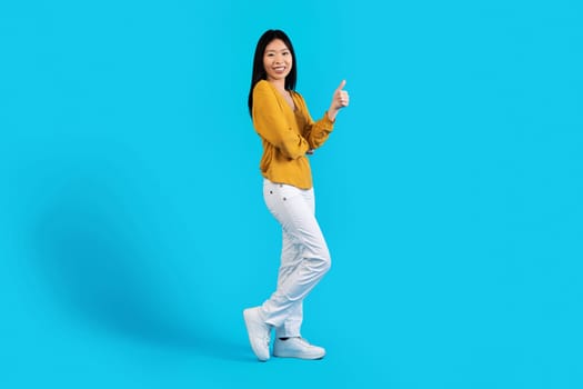 Cheerful beautiful korean woman showing thumb up, blue background