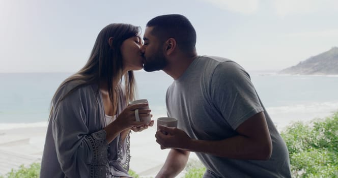 Couple, kiss and coffee in morning on balcony with love, romance and care on holiday by ocean with sunshine. Man, woman and trust with drink, espresso or matcha on vacation by sea with bond in summer.