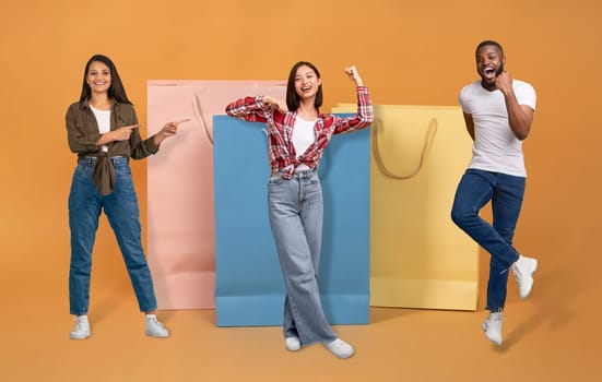 Concumerism concept. Cheery happy beautiful multiethnic young people man and women in casual posing by big shopping bags over colorful background, collage. Shopaholics enjoying season sale