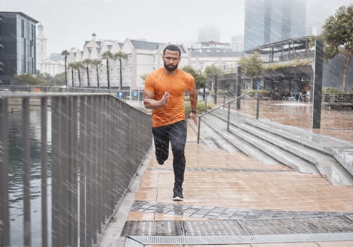 City fitness, man and running in rain for exercise, body workout and cardio training. Portrait, wet and urban runner with focus, motivation and strong motivation for sports, power and marathon energy
