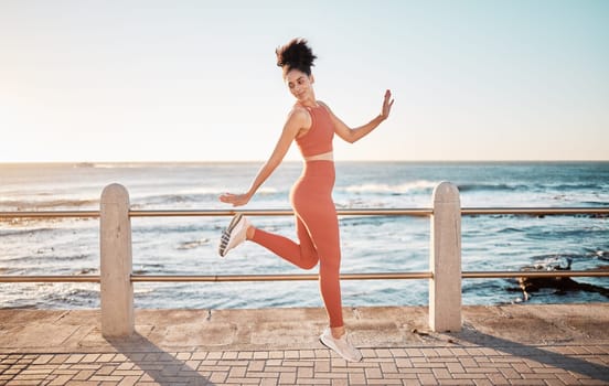 Fitness, happy running and woman jumping on beach path on fun morning exercise with freedom and happiness. Run, jump and smile, excited girl on healthy ocean walk with joy, wellness and workout goals