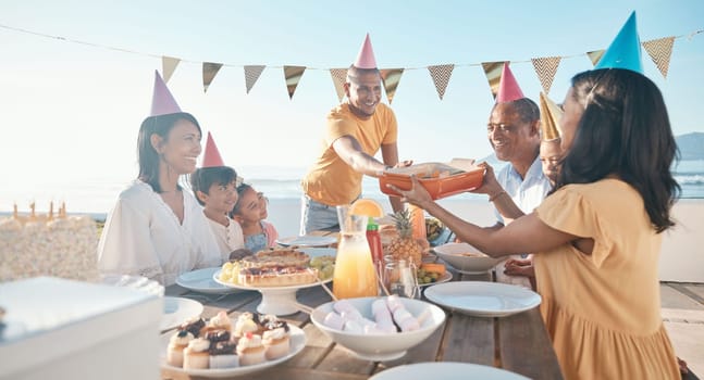 Birthday, parents and children with food by beach for event, celebration and party outdoors. Family, social gathering and mother, father with kids at picnic with cake, presents and eating together