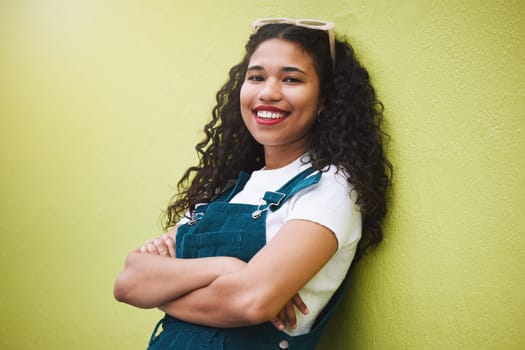 Girl smile with fashion glasses in hair, show expression of beauty, happiness and confidence. Portrait of beautiful latino woman, happy with arms crossed against green background or wall in the city