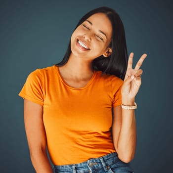 Happy woman with smile, peace hand sign and Gen z youth, freedom and fashion isolated on studio background. Happiness, mindset and v emoji, beauty with young person, eyes closed and care free.