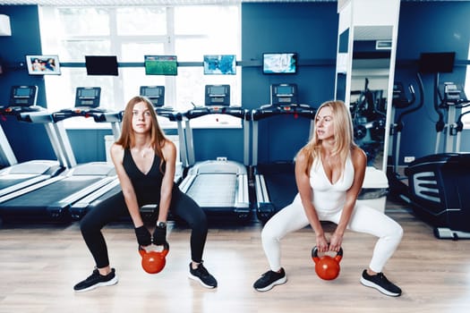 Mother and daughter in sportswear exercising with dumbbells in the gym
