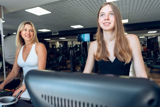 Mother and teen daughter in sportswear exercise on treadmill at the gym