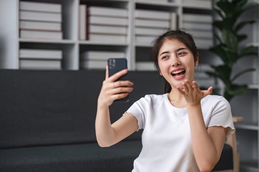Shot of a happy young Asia woman taking selfie with her cellphone while sitting at living room.