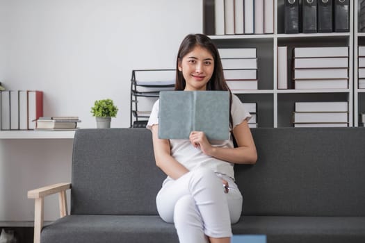 Attractive young Asian woman sits in the minimal and comfortable living room enjoying reading a book.