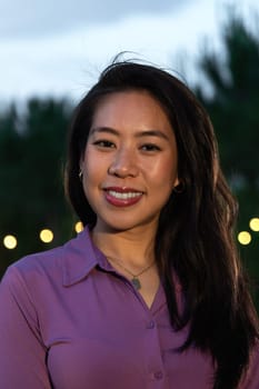 Vertical headshot of young smiling asian woman at sunset.